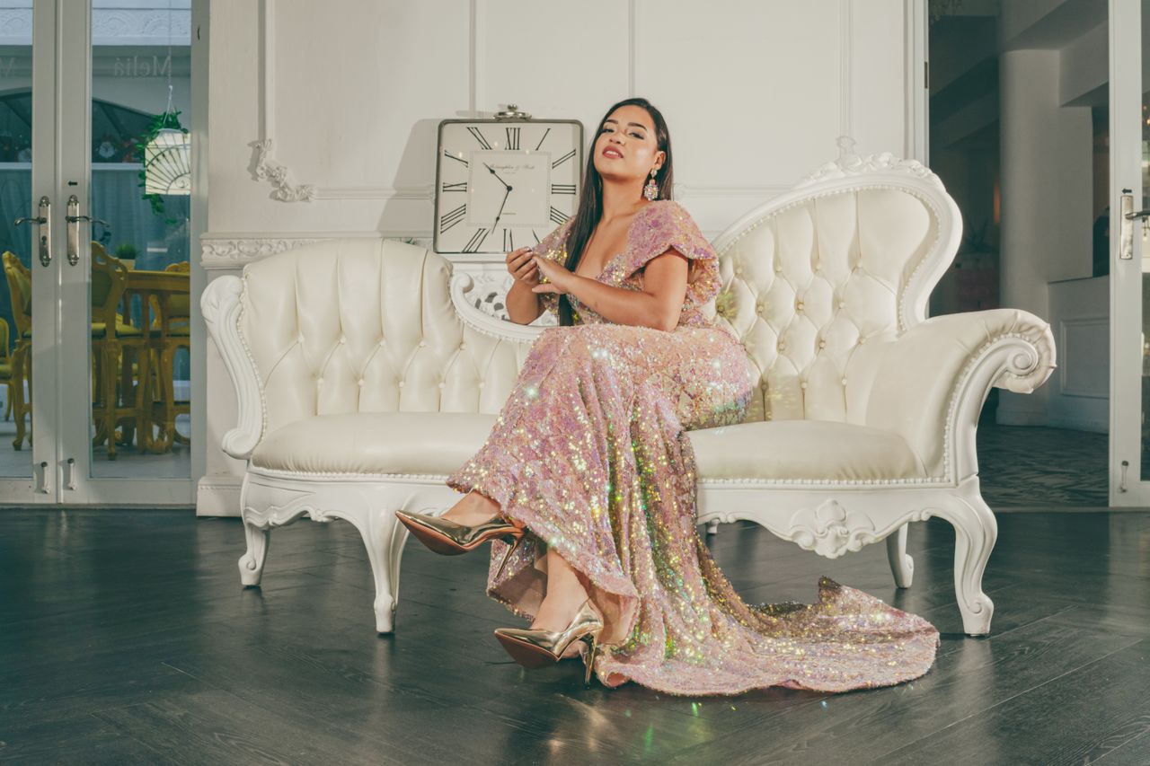 services-02 Portrait of a woman in a sparkling dress sitting on an elegant white sofa indoors.